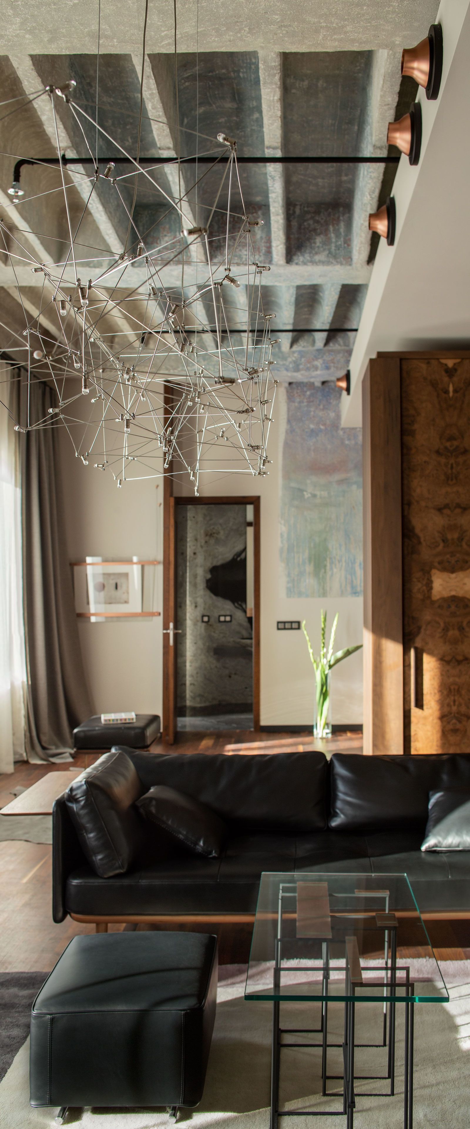 Una sala de estar moderna con un sofá de cuero negro, una mesa de centro de vidrio y una lámpara colgante.