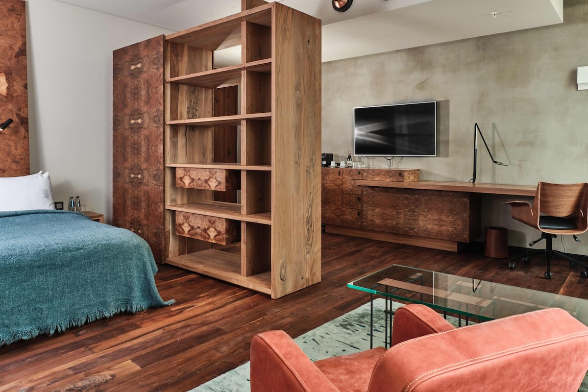 A modern bedroom with a wooden bookshelf, a glass coffee table, a sofa, and a desk with a TV.