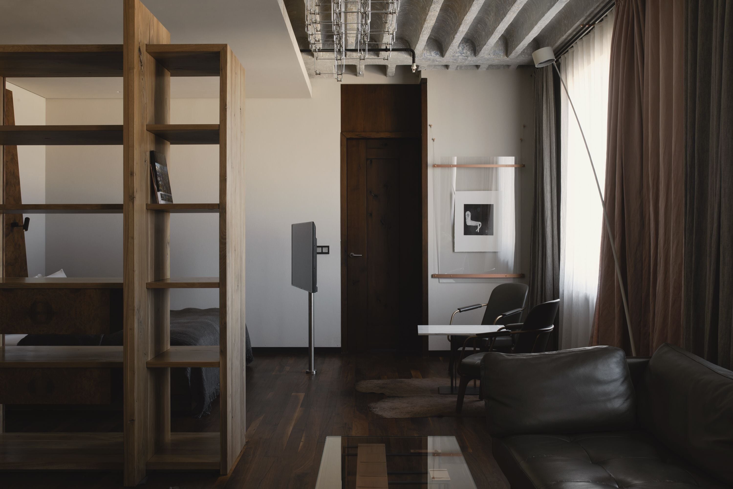 Una habitación moderna con una estantería de madera, un escritorio, un sofá de cuero y un ventanal con cortinas.