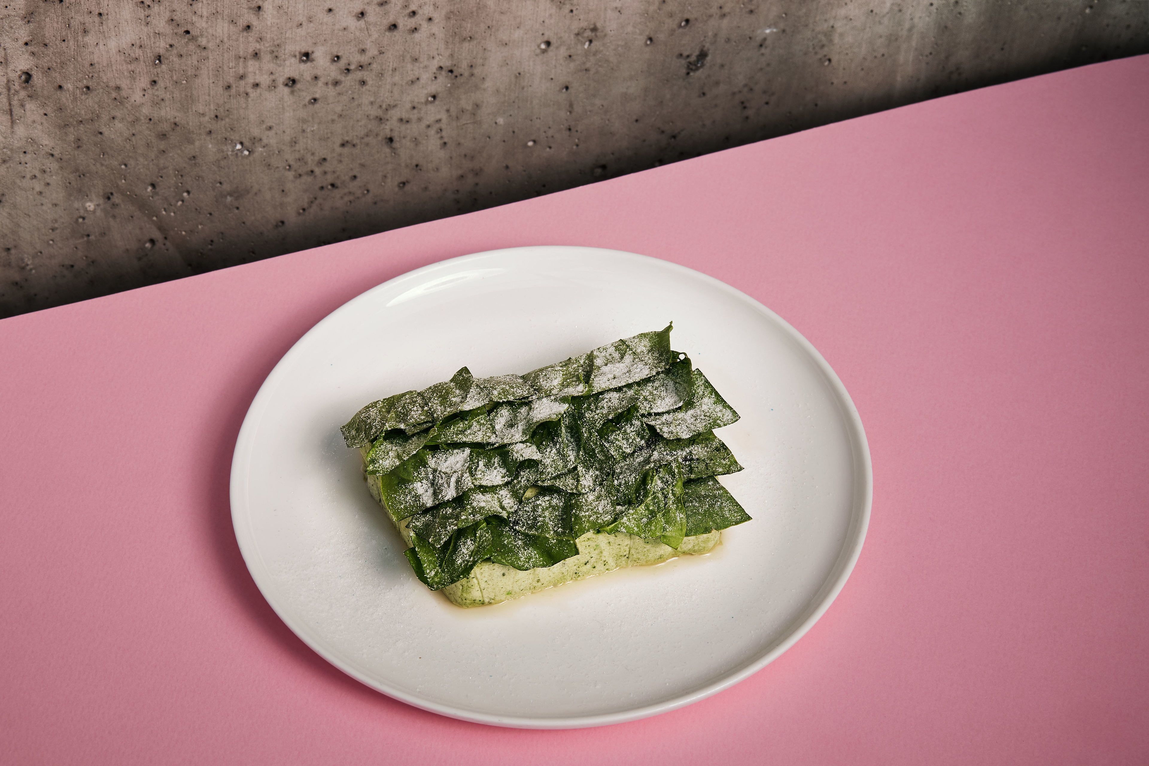 A plate with a rolled pastry on a white plate, set on a pink surface.