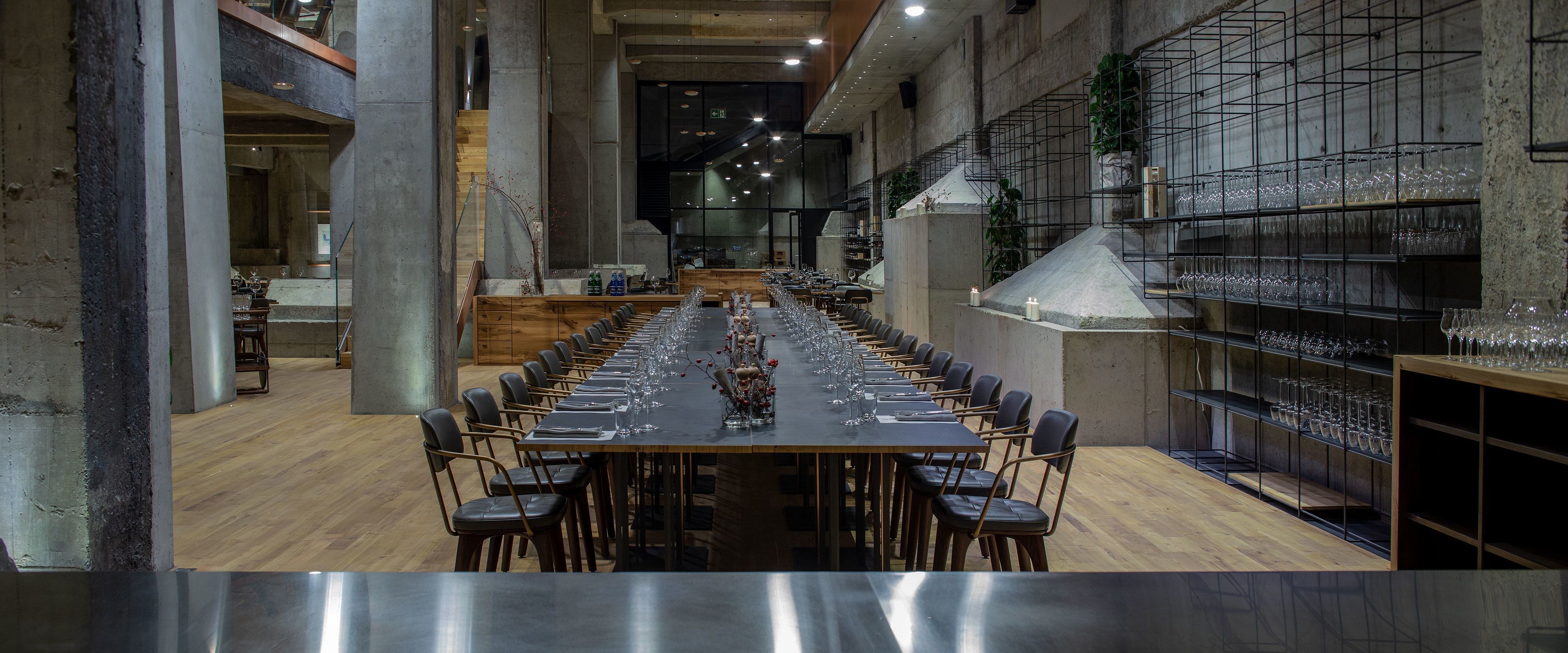 Una larga mesa de comedor con sillas, rodeada de estantes llenos de copas y botellas de vino.