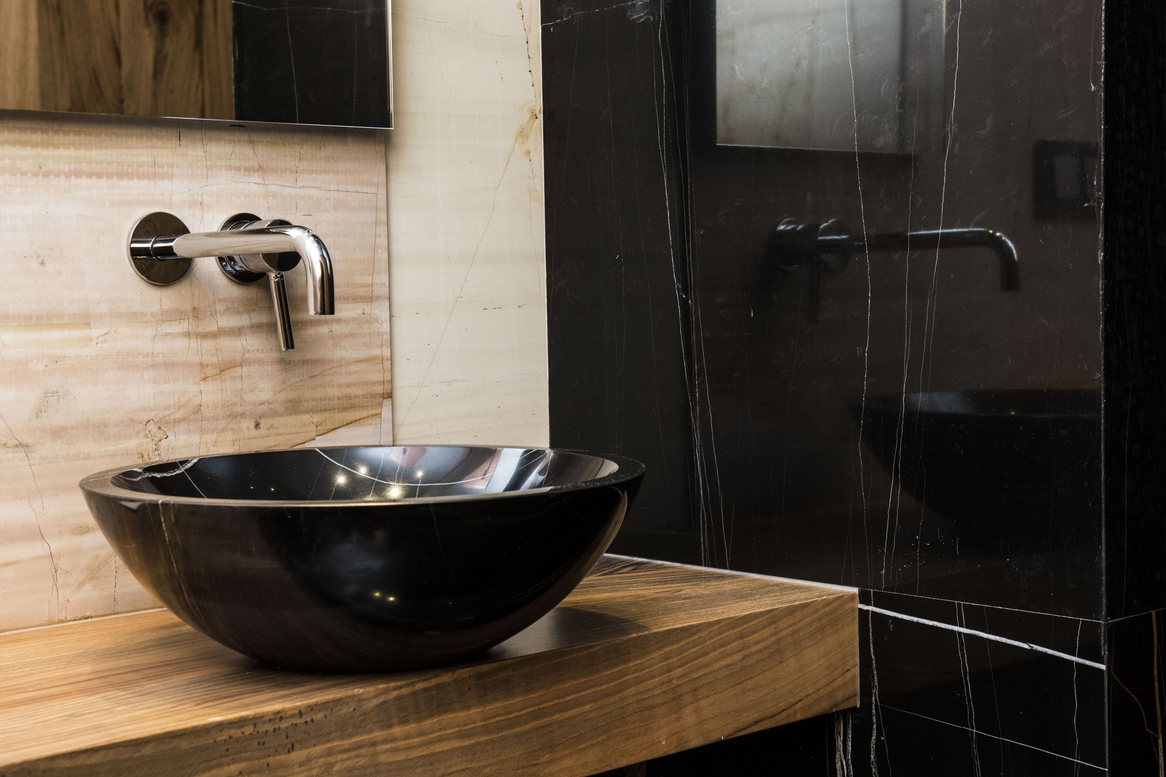 A modern bathroom with a wooden vanity, a black marble sink, and a glass shower enclosure.
