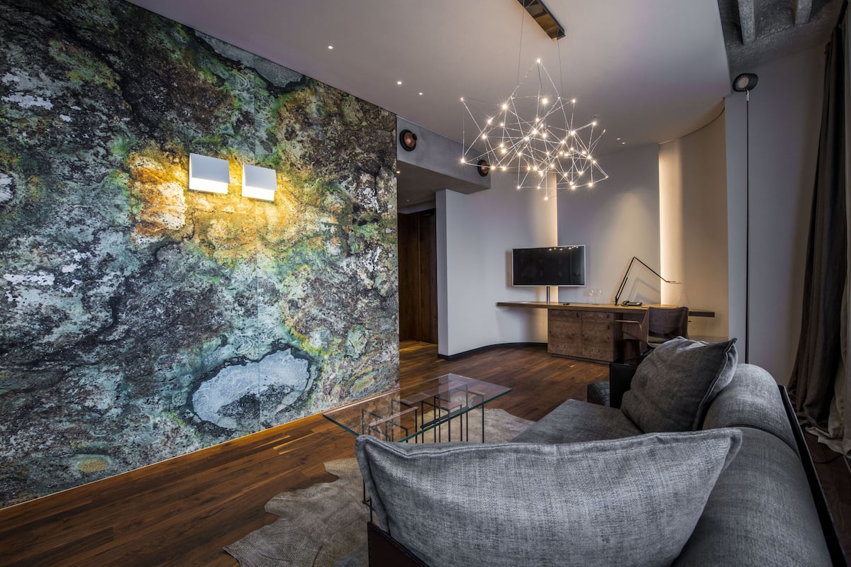 A modern living room with a textured wall, a glass coffee table, a grey sofa, and a contemporary light fixture.