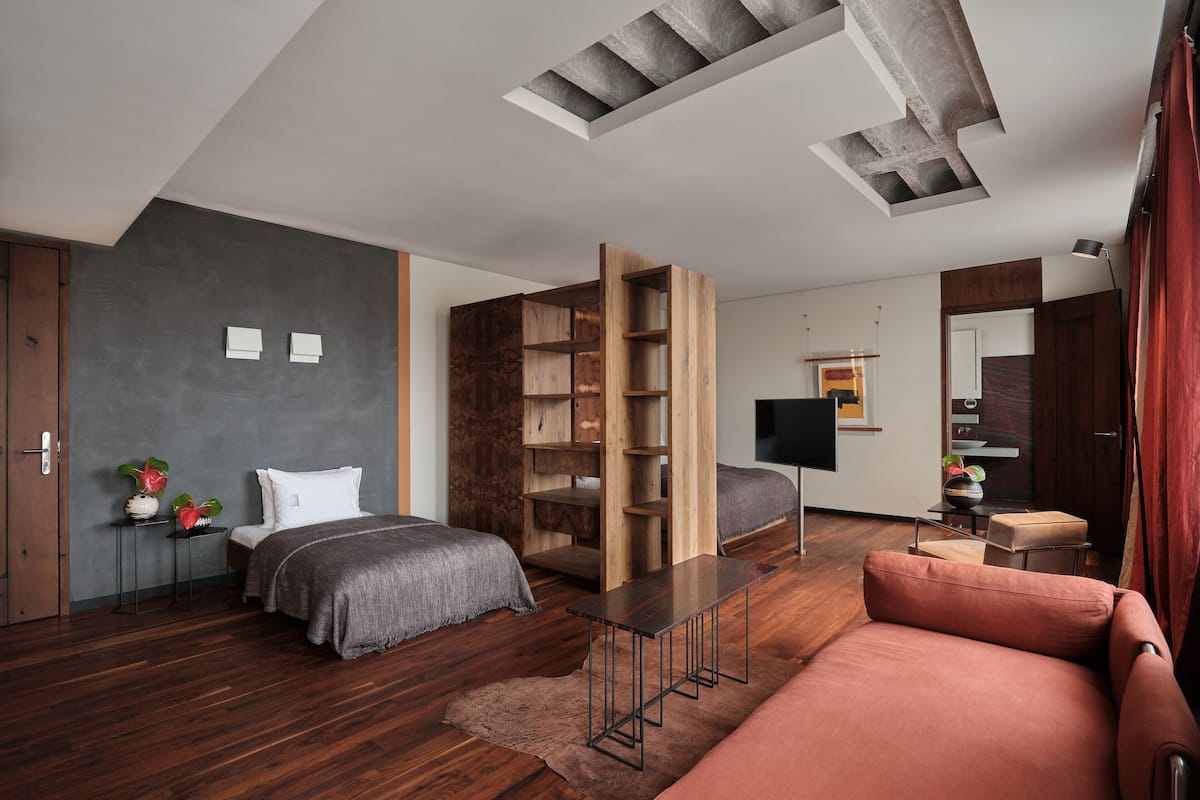 A modern bedroom with a bed, a sofa, a wooden bookshelf, and a desk.