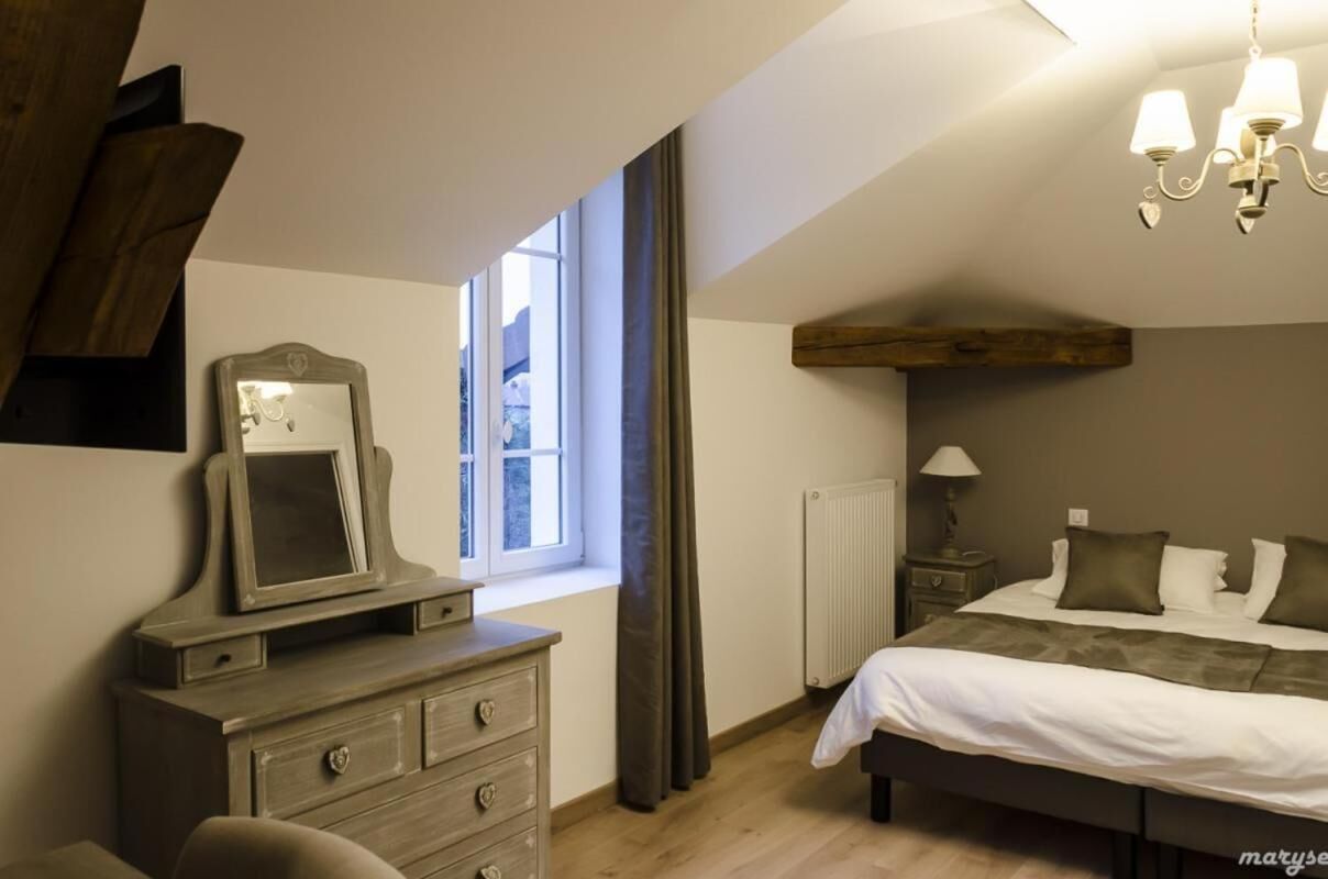 Een slaapkamer met een bed, een linnenkast, een spiegel, een raam met gordijnen, een radiator en een kroonluchter.