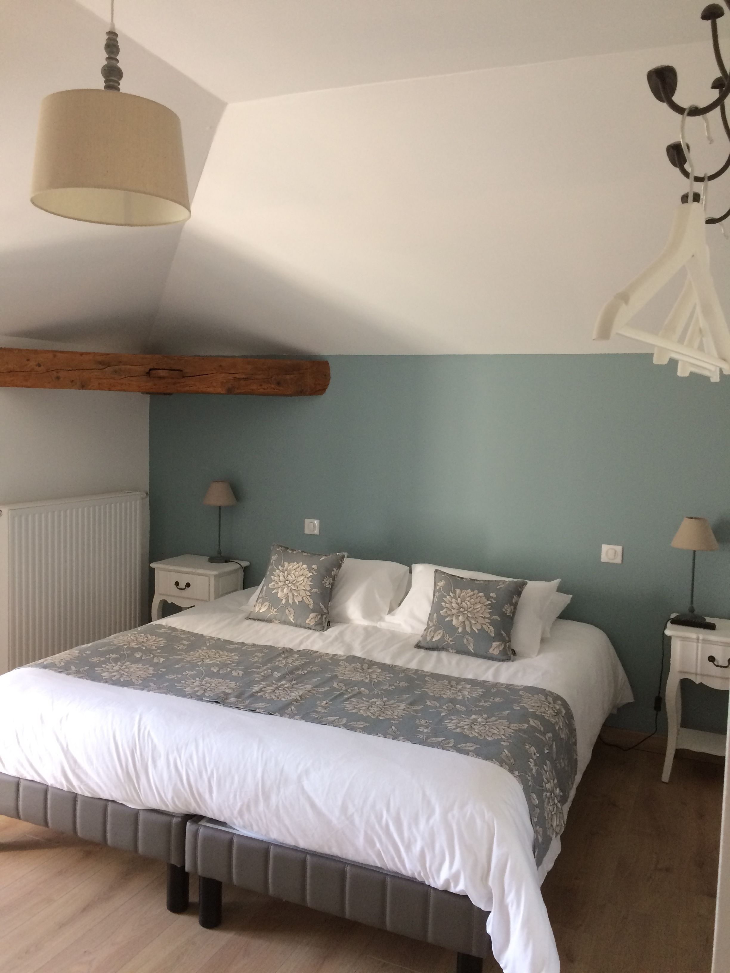Un dormitorio con cama, mesitas de noche, lámpara colgante y techo con vigas de madera.