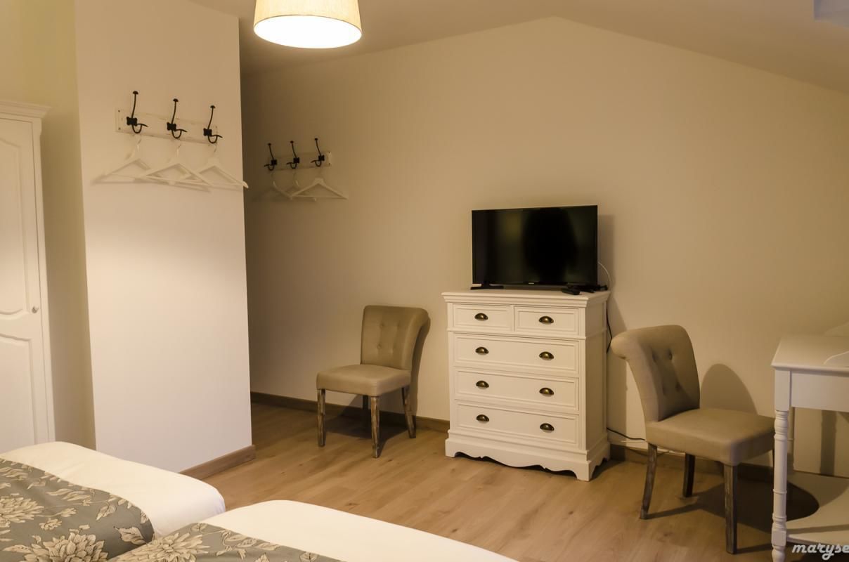 A hotel room with a bed, two chairs, a dresser, a TV, and a coat rack with hangers.