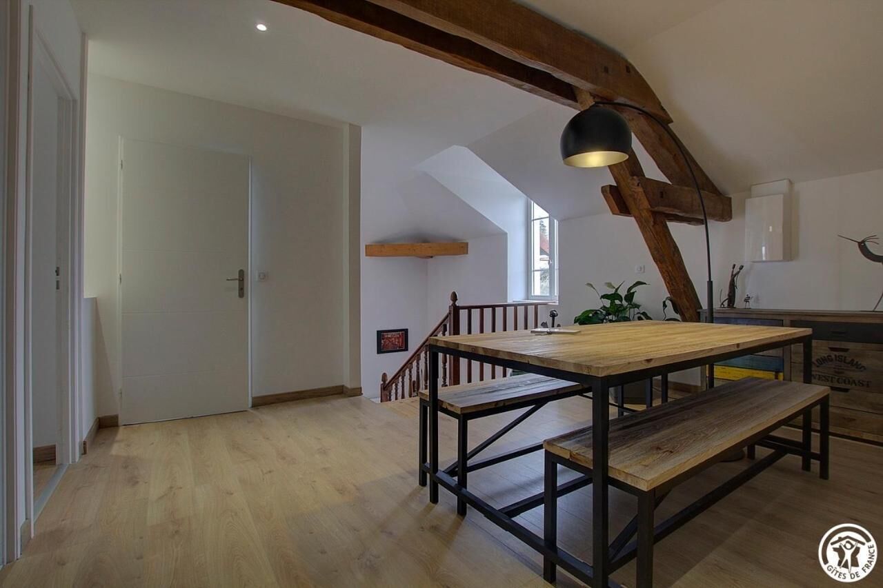 A spacious room with a wooden dining table and benches, a staircase, and a large window providing natural light.