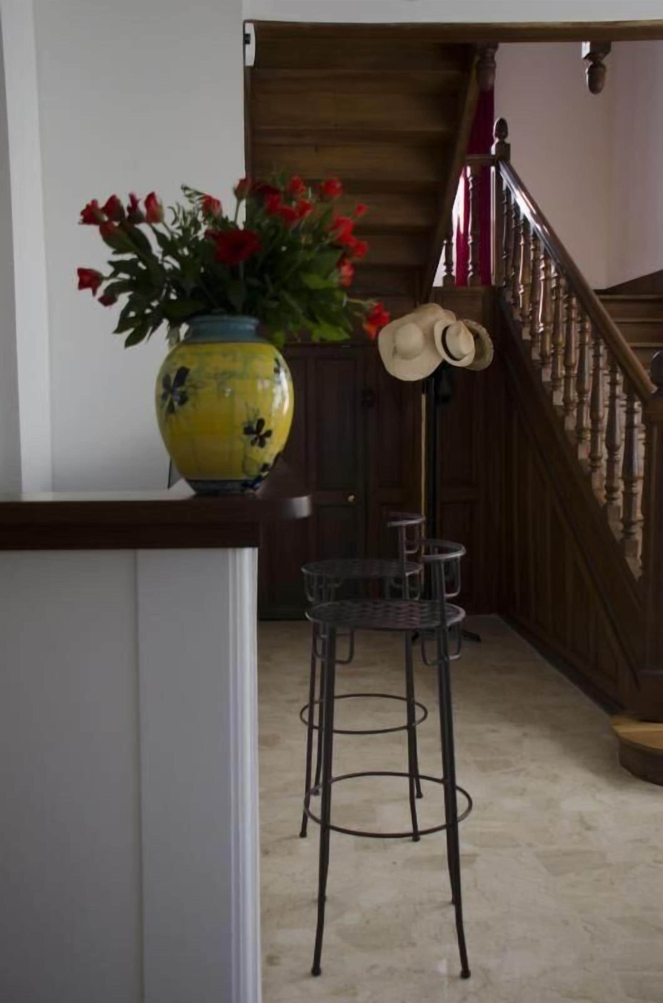 A staircase with a wooden railing and a vase of red flowers on a counter.