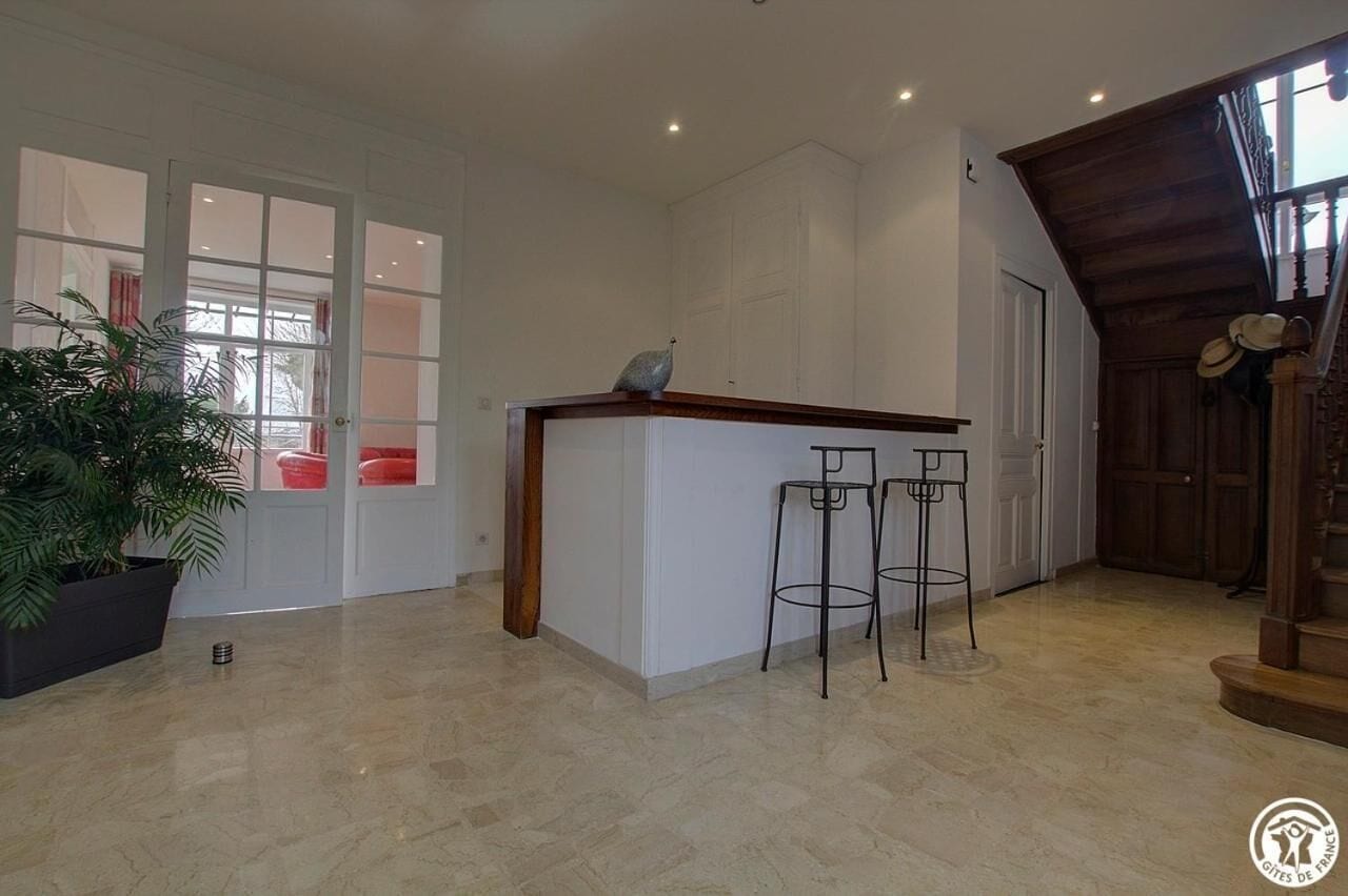 Une pièce spacieuse avec un îlot de cuisine, deux tabourets de bar, une plante en pot et un escalier.