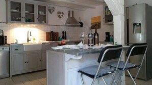 Una cocina con armarios blancos, una isla central con taburetes de bar, un fregadero y un refrigerador.