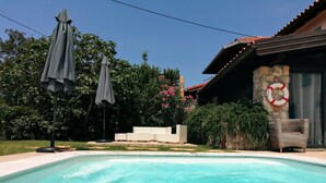 Una piscina con un muro de piedra y un flotador salvavidas. Hay dos sombrillas y una silla de mimbre.