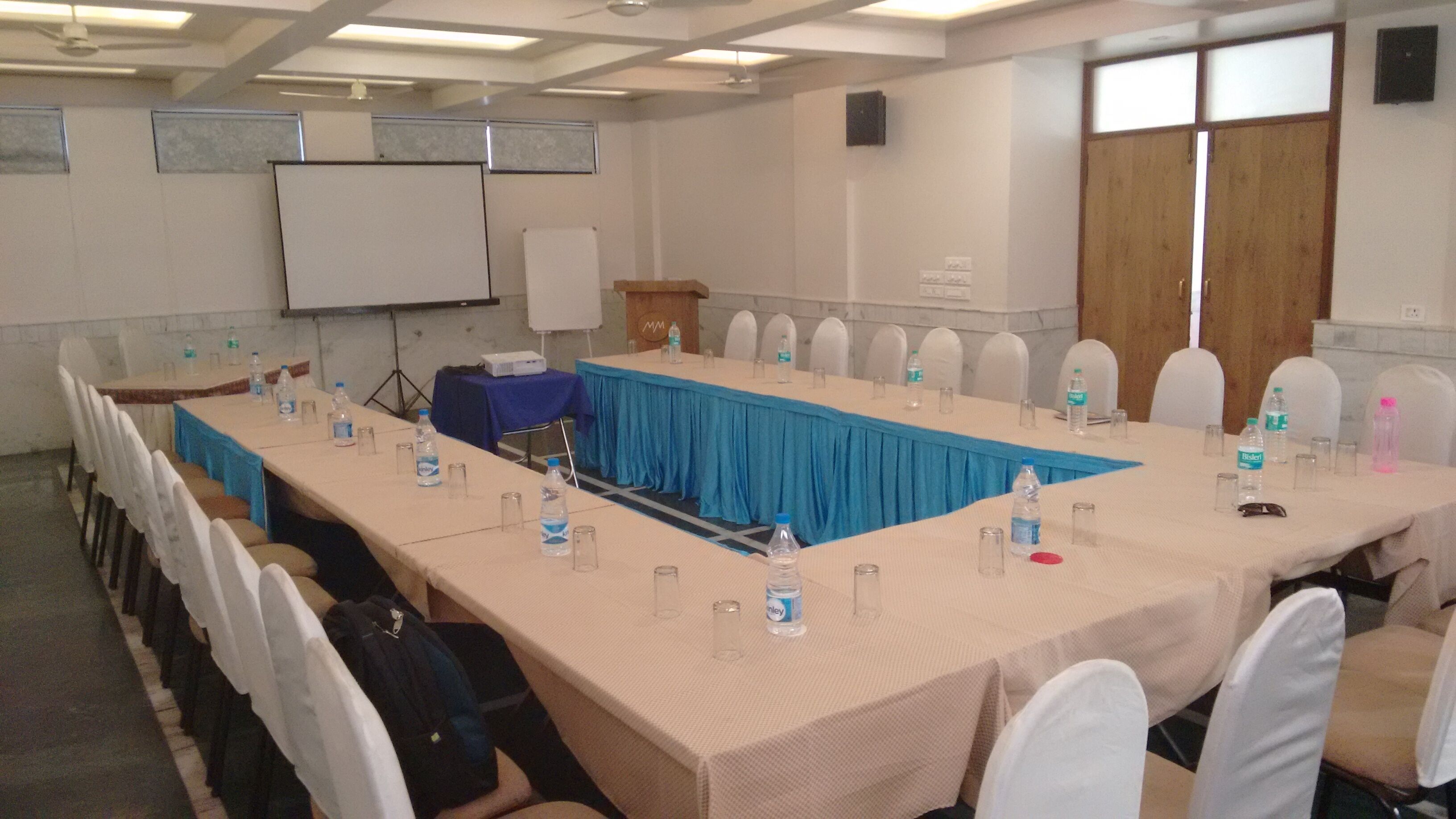 A conference room with a long table, chairs, water bottles, and a projector screen.