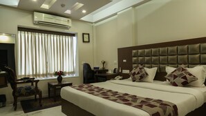 A hotel room with a large bed, a desk, a chair, an air conditioner, and a window with curtains. - The Majestic Manor (Nagpur)
