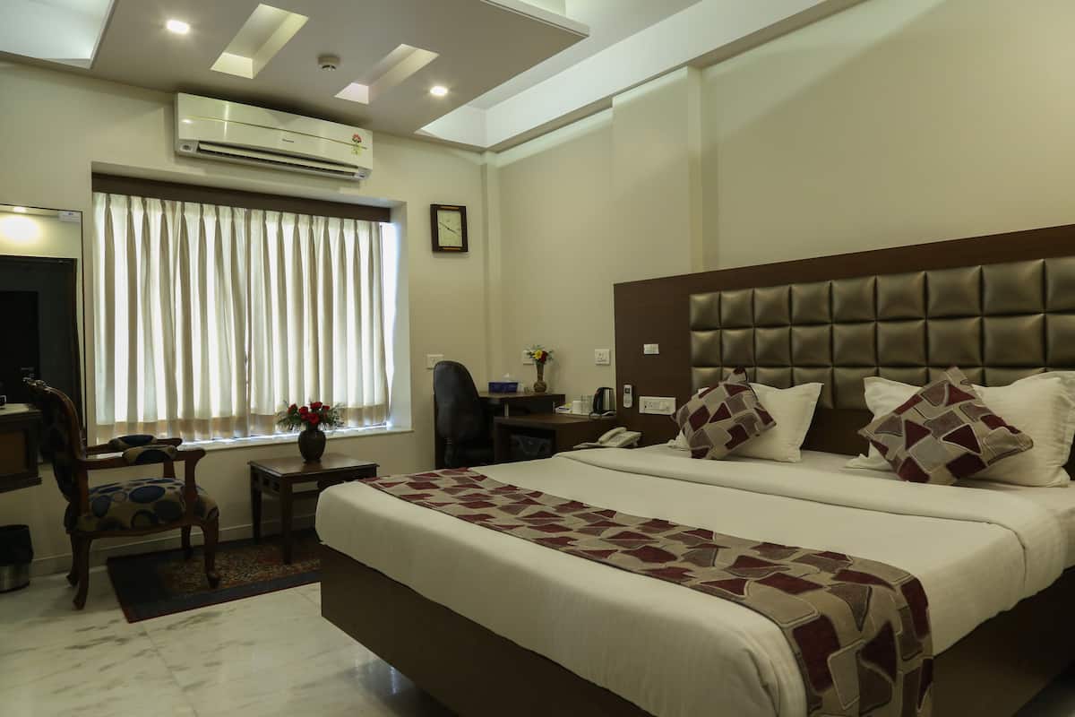 Habitación de hotel con una cama grande, un escritorio, una silla, aire acondicionado y una ventana con cortinas.