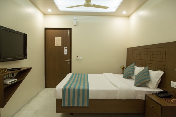 Una habitación de hotel con cama, mesita de noche, televisión y ventilador de techo.