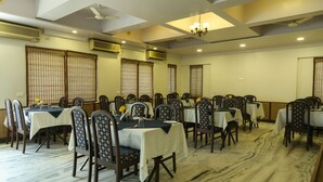A dining area with multiple tables and chairs, air conditioning units, and a chandelier. - The Majestic Manor (Nagpur)