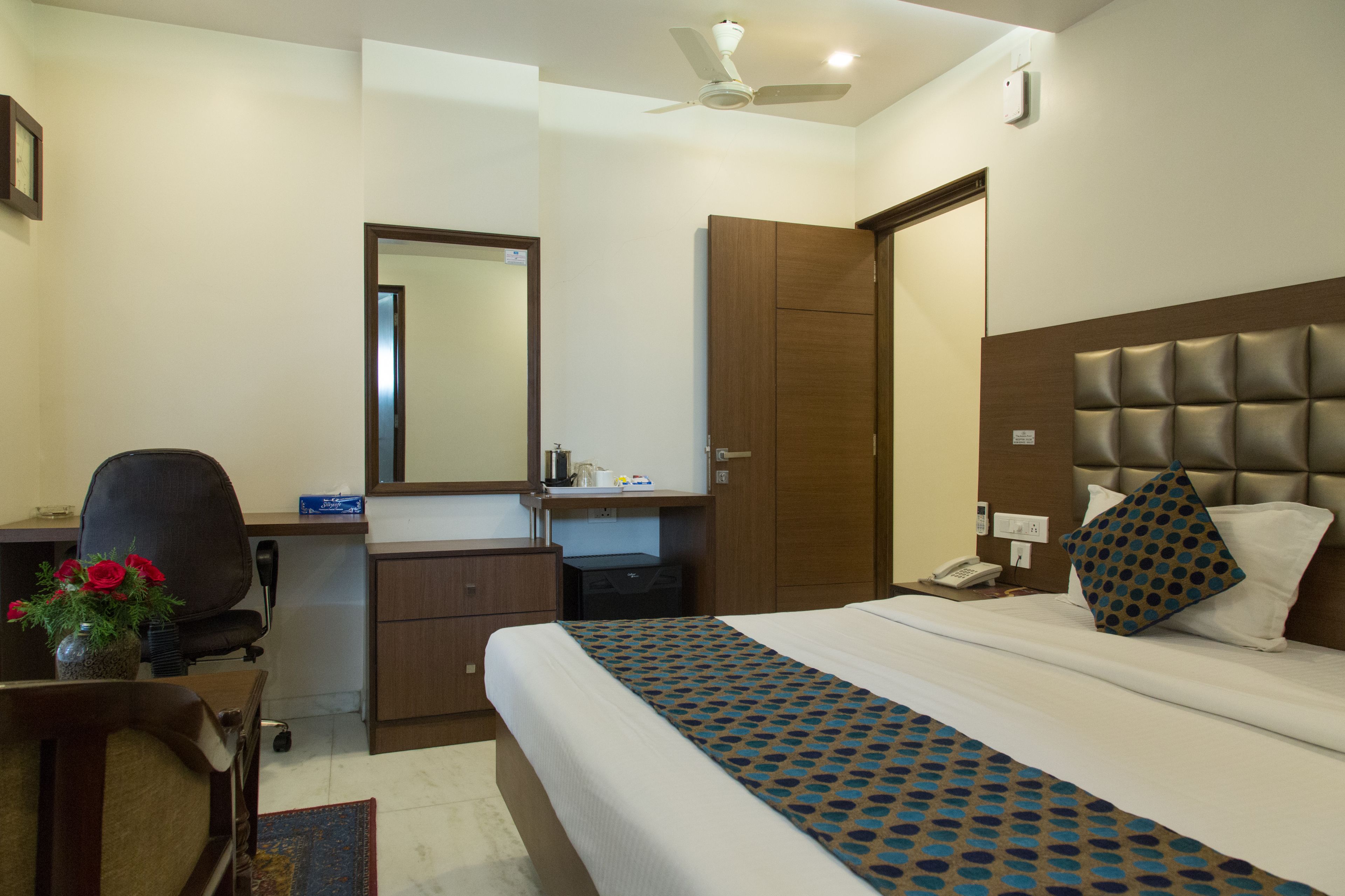 A hotel room with a bed, desk, chair, and a mirror.