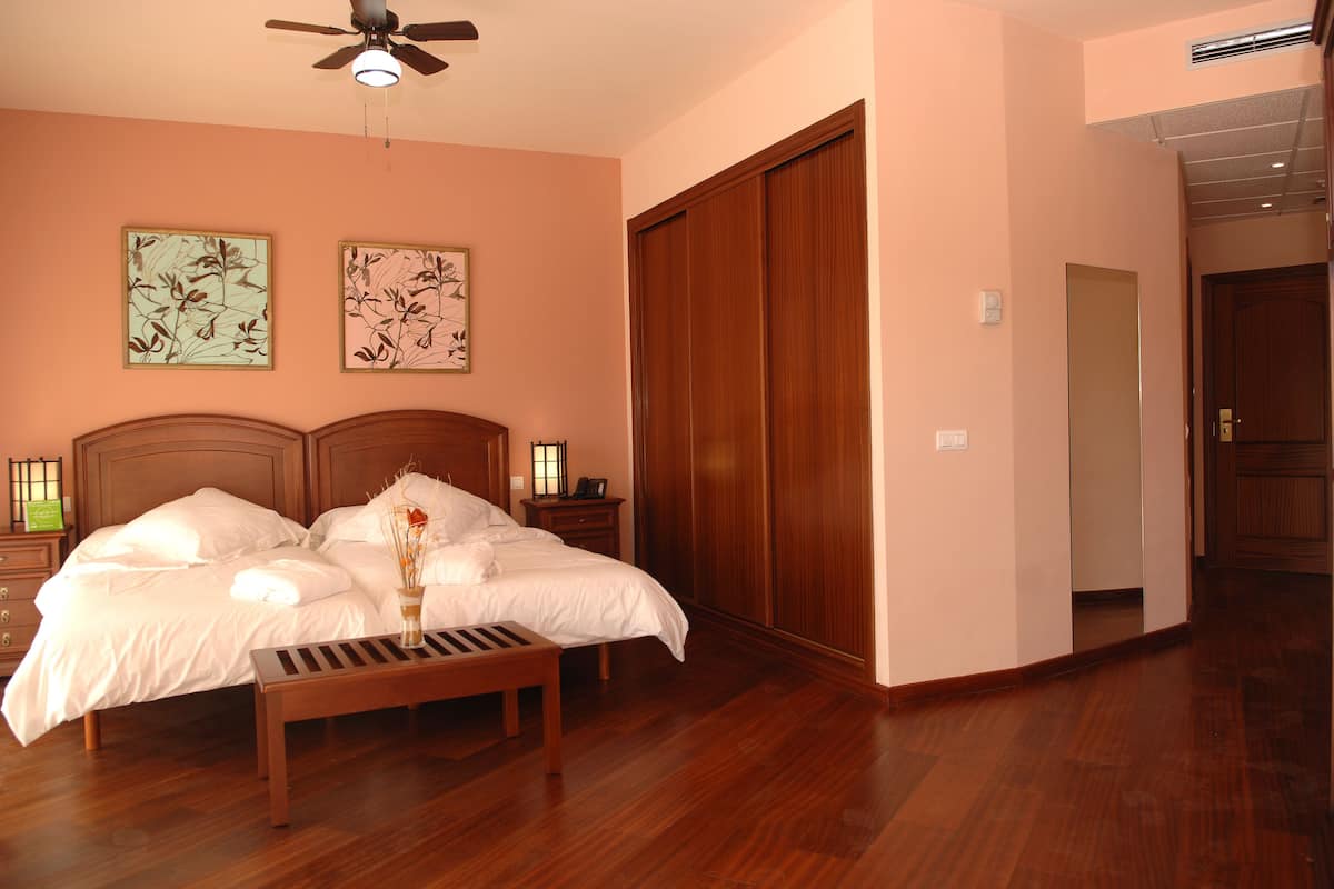 A bedroom with a wooden bed, a nightstand, a bench, two wall-mounted lamps, and a ceiling fan.