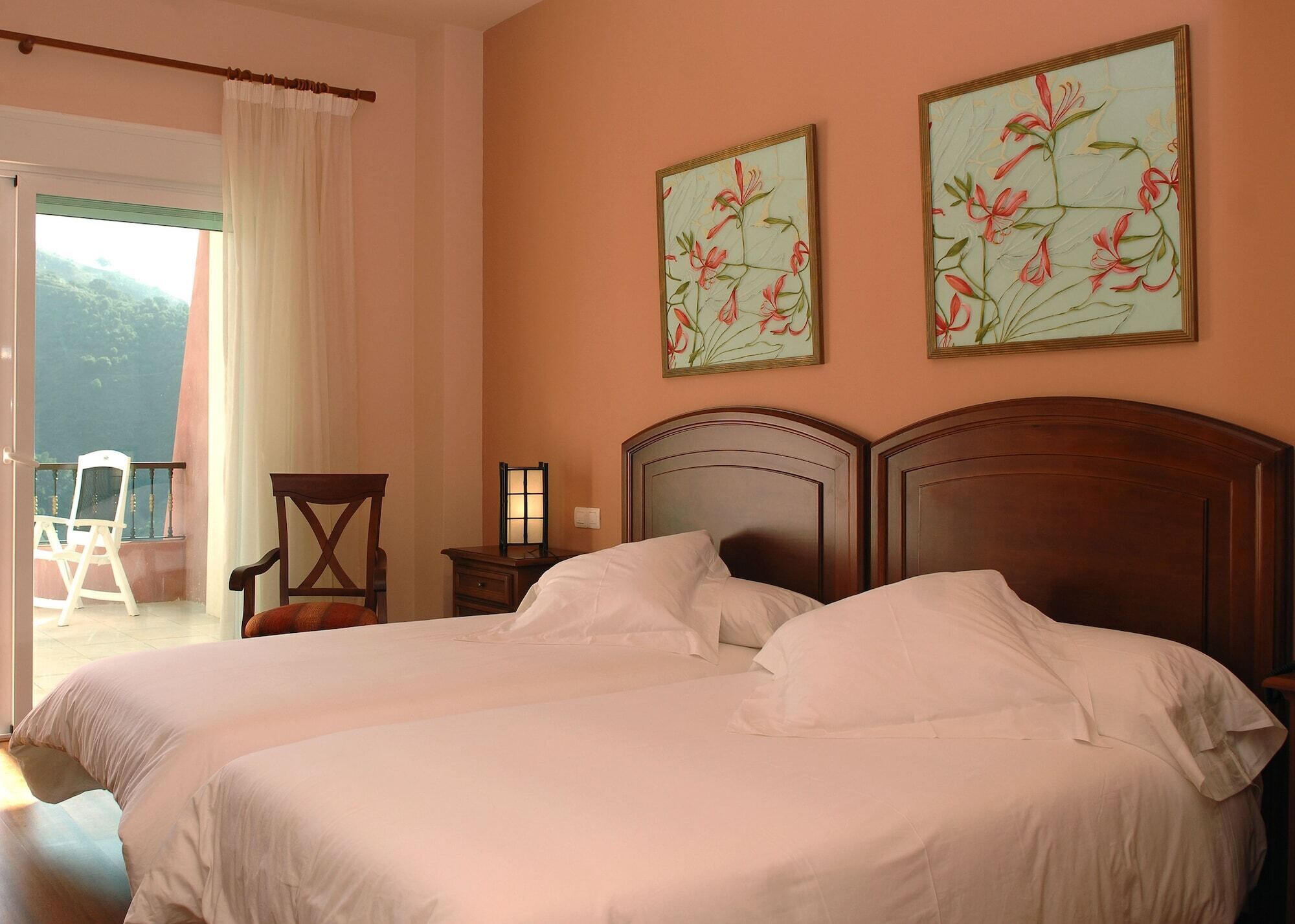A double bed with white linens, a wooden headboard, and two floral paintings on the wall.