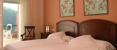 A double bed with white linens, a wooden headboard, and two floral paintings on the wall.