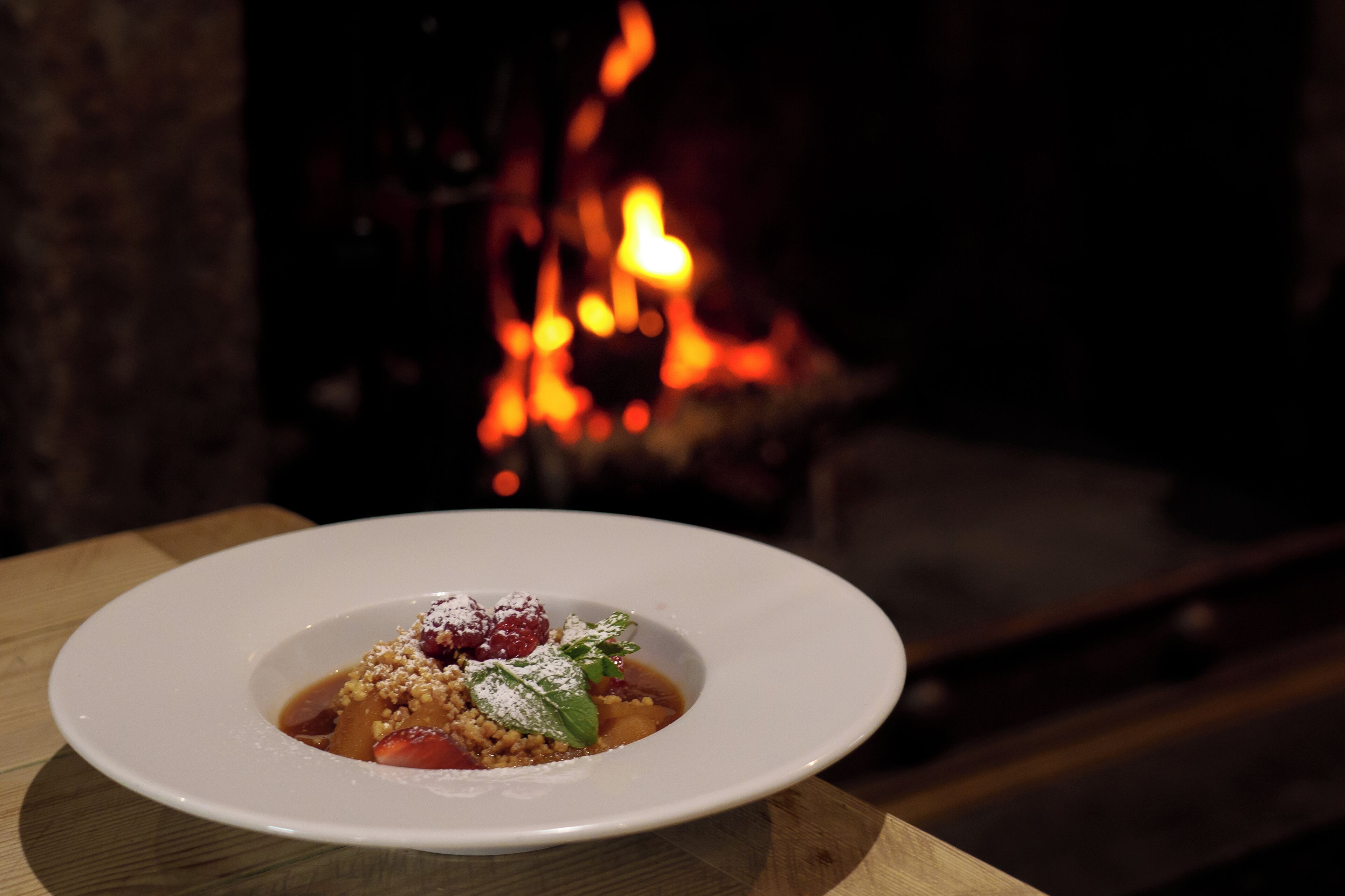 A white plate with a dessert on a wooden table, with a fireplace in the background.