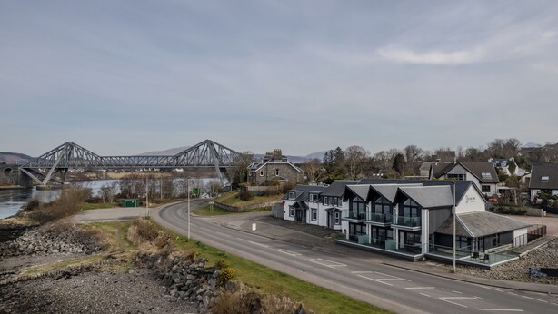 A modern hotel with a glass facade, located near a river and a bridge.