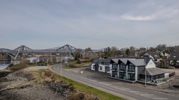 A modern hotel with a glass facade, located near a river and a bridge.