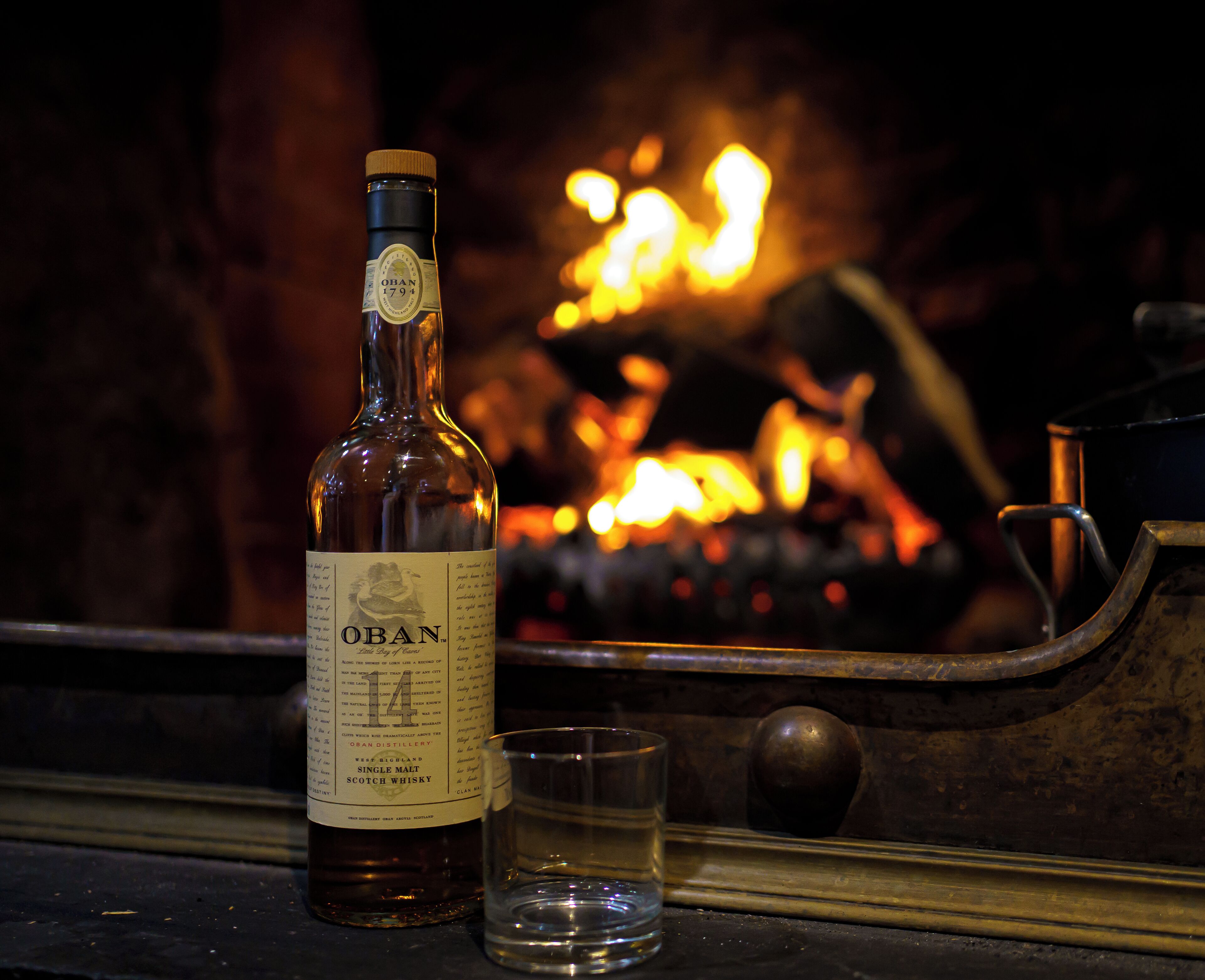 A bottle of OBN Scotch whisky and a glass on a wooden surface with a fireplace in the background.