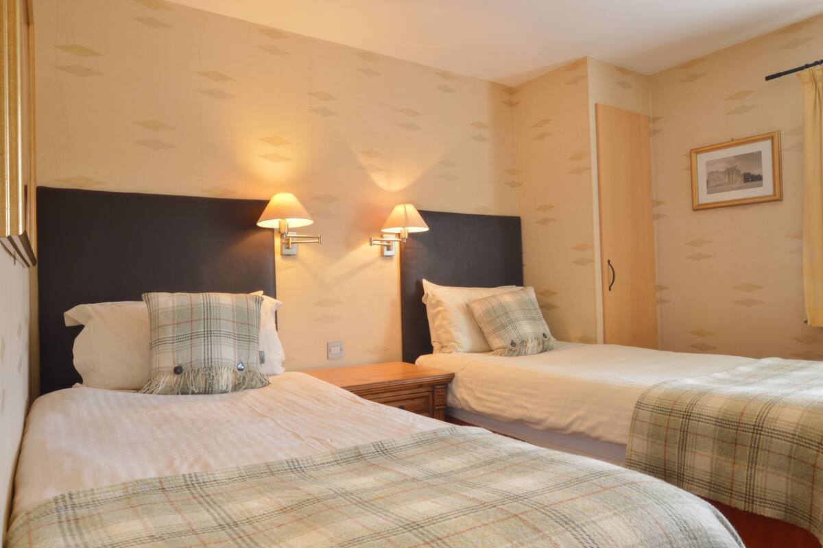 A hotel room with two beds, a headboard, wall-mounted lamps, a framed picture, and a door.