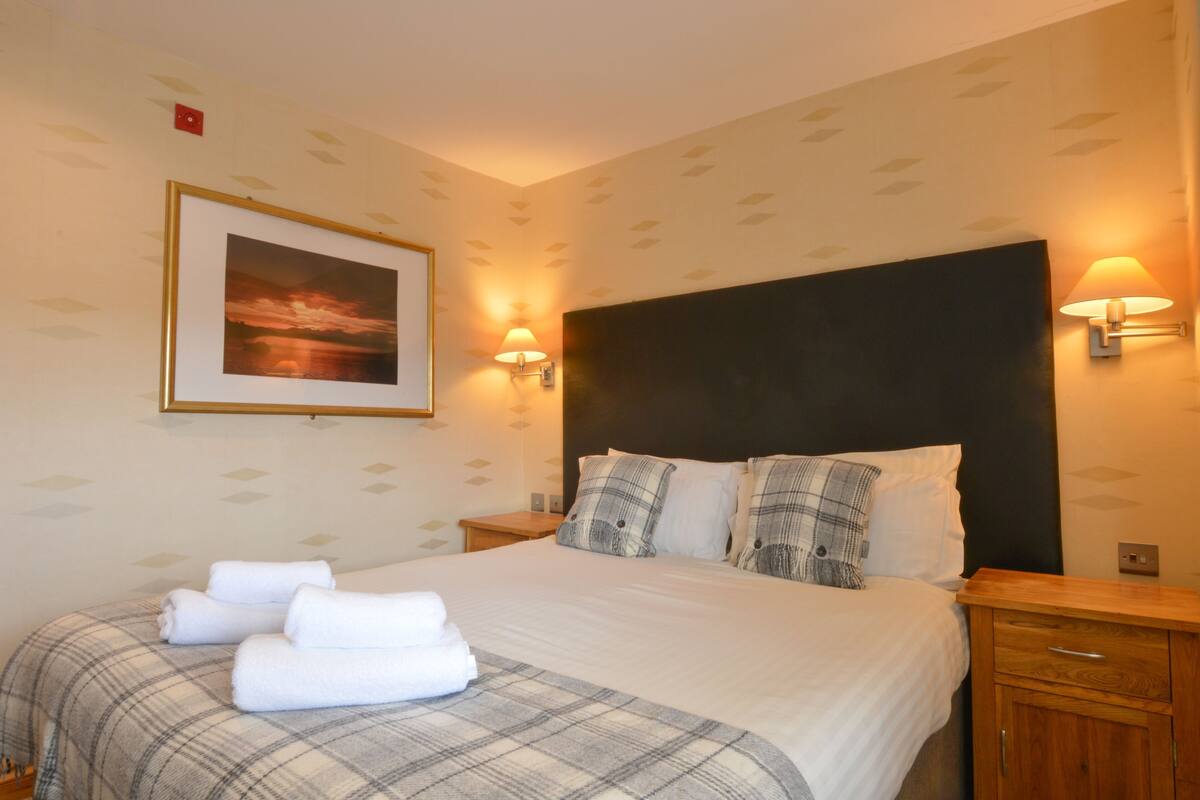 A hotel room with a bed, two bedside lamps, a framed picture on the wall, and a nightstand with a lamp.