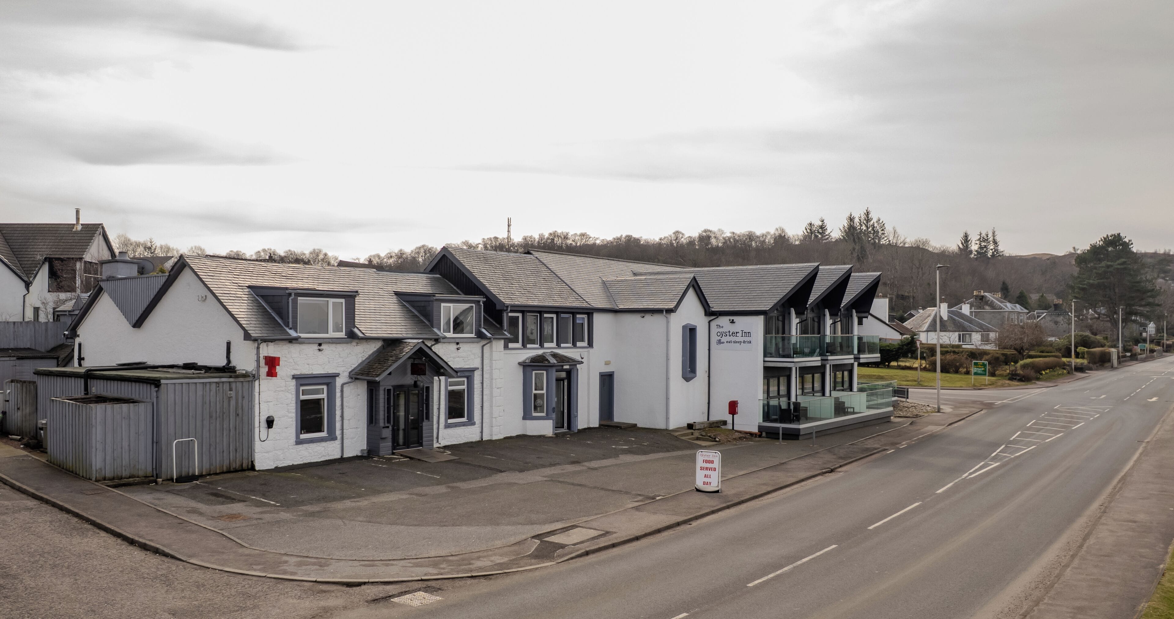 Een rij witte gebouwen met grijze daken, een bord met 'The Oyster Inn' en een bord waarop staat 'Food Served All Day'.