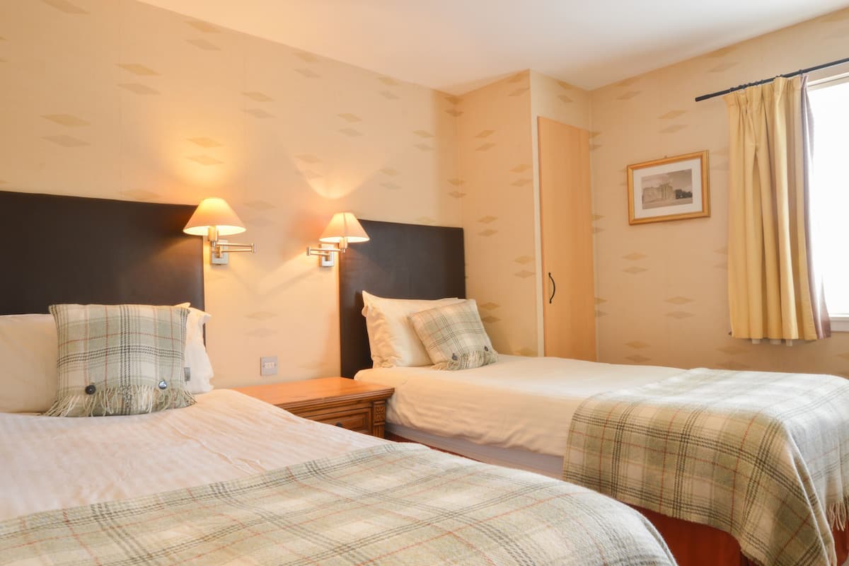 A hotel room with two beds, a headboard, wall-mounted lamps, a framed picture, and a window with curtains.