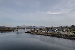 A river with a bridge, houses, and mountains in the background.