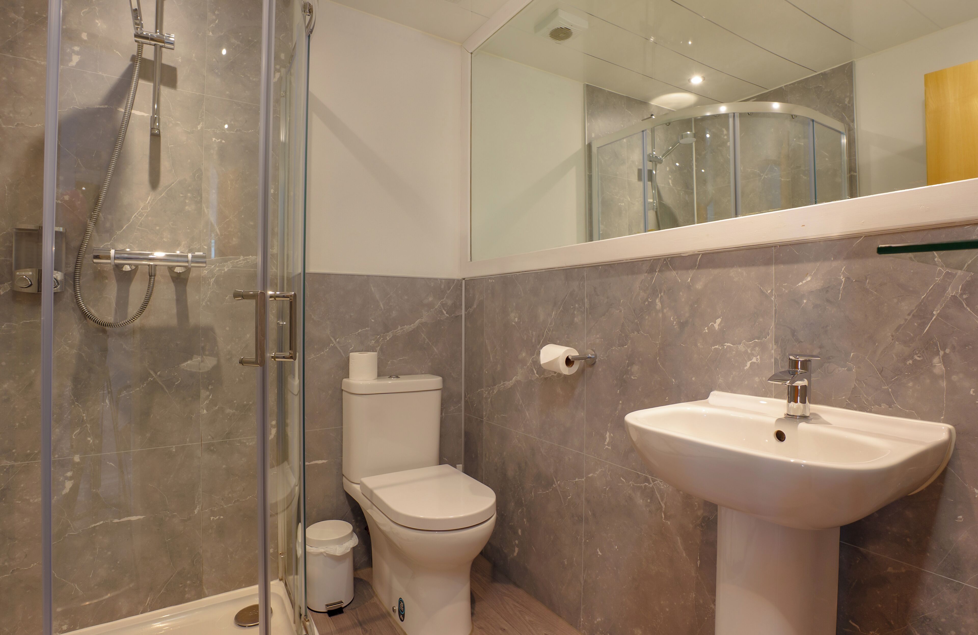 A modern bathroom with a glass-enclosed shower, a toilet, and a pedestal sink.
