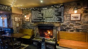 A cozy pub with a stone wall, a fireplace, and a menu board.