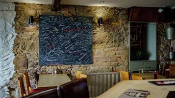Ein Restaurantinneres mit einer Kreidetafel-Speisekarte, Steinwänden, Holzmöbeln und einem sichtbaren Küchenbereich.