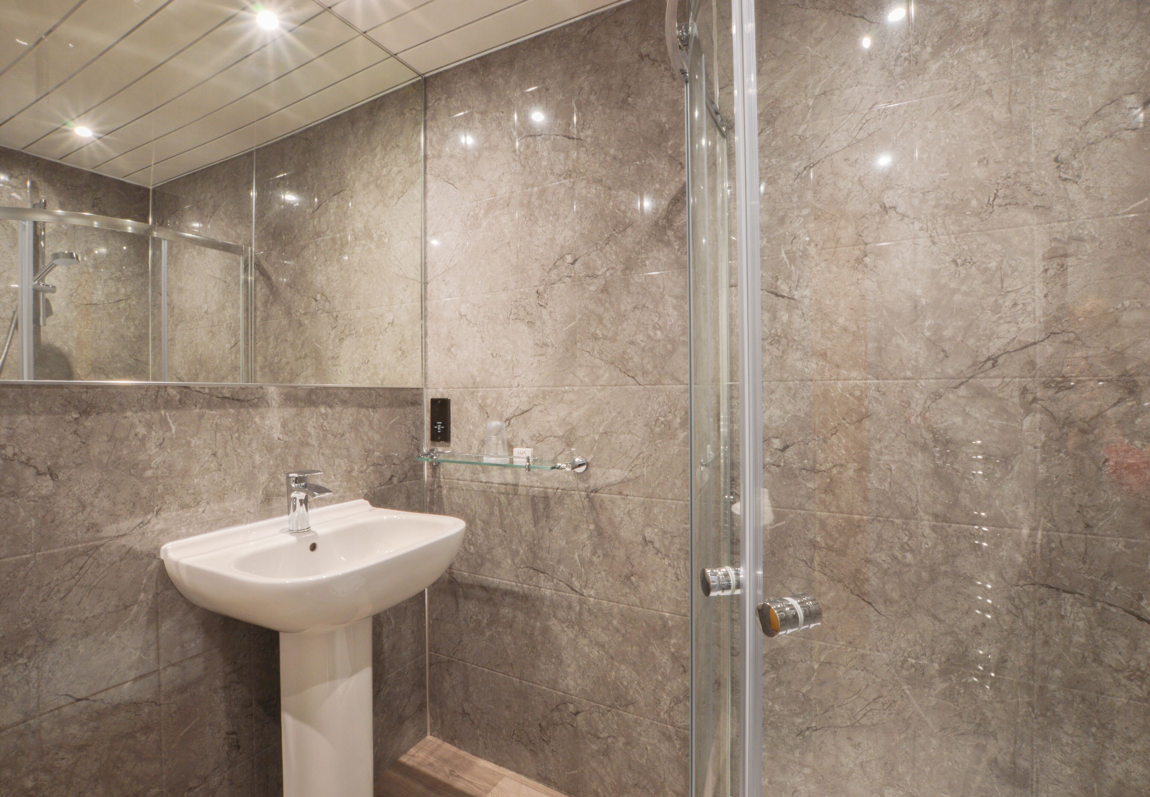 A bathroom with a white pedestal sink, a glass shower enclosure, and marble walls.