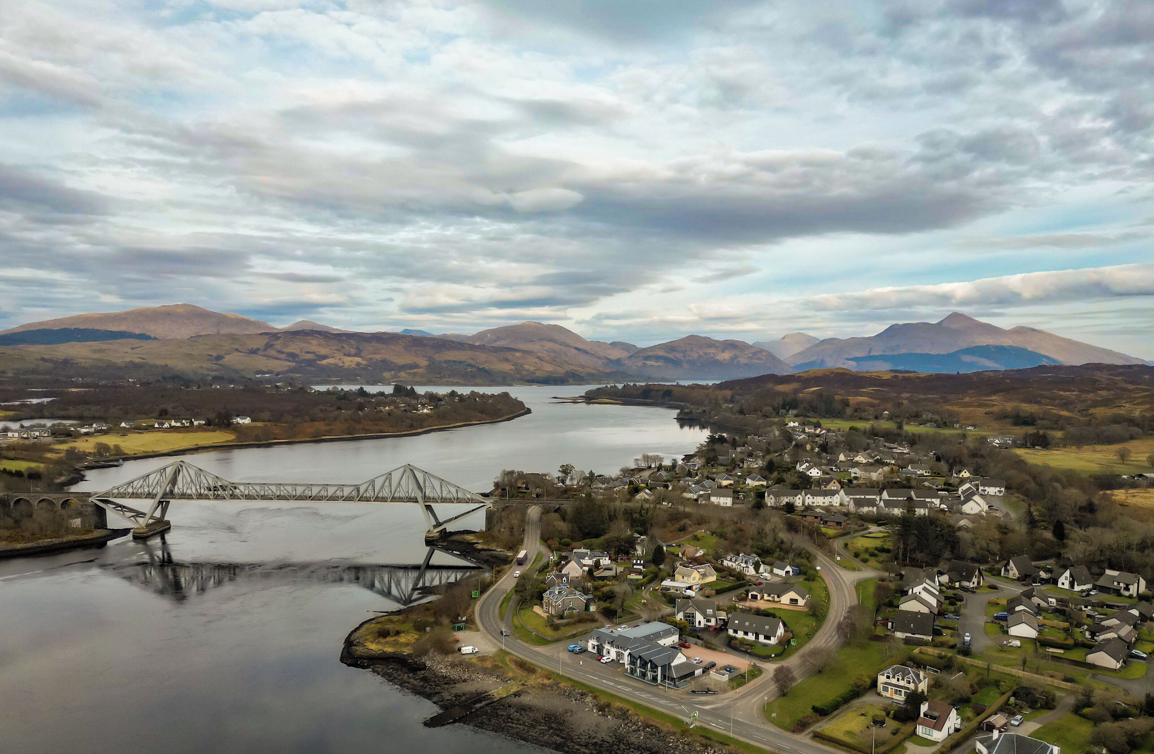 A bridge over a river with a town in the foreground and mountains in the background.