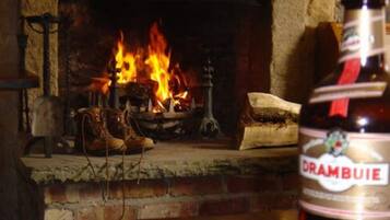 Uma lareira com lenha ardendo, uma garrafa de Drambuie e um par de botas na peça sobre a lareira.