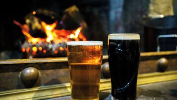 Two glasses of beer on a bar counter with a fire in the background.