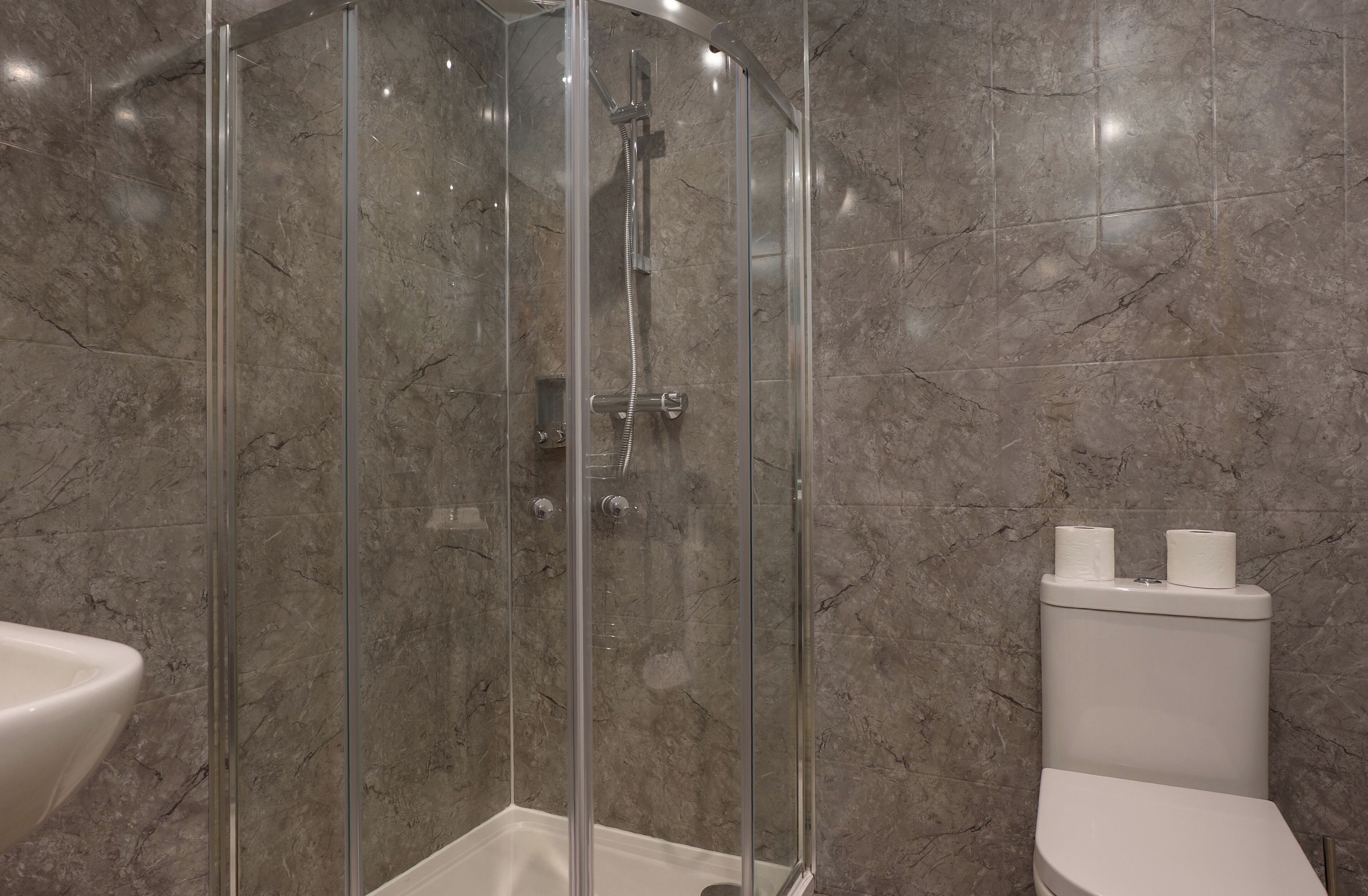 A modern bathroom with a glass-enclosed shower, a white toilet, and a sink.
