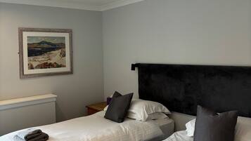 A hotel room with two beds, a headboard, a painting on the wall, and a ceiling light.