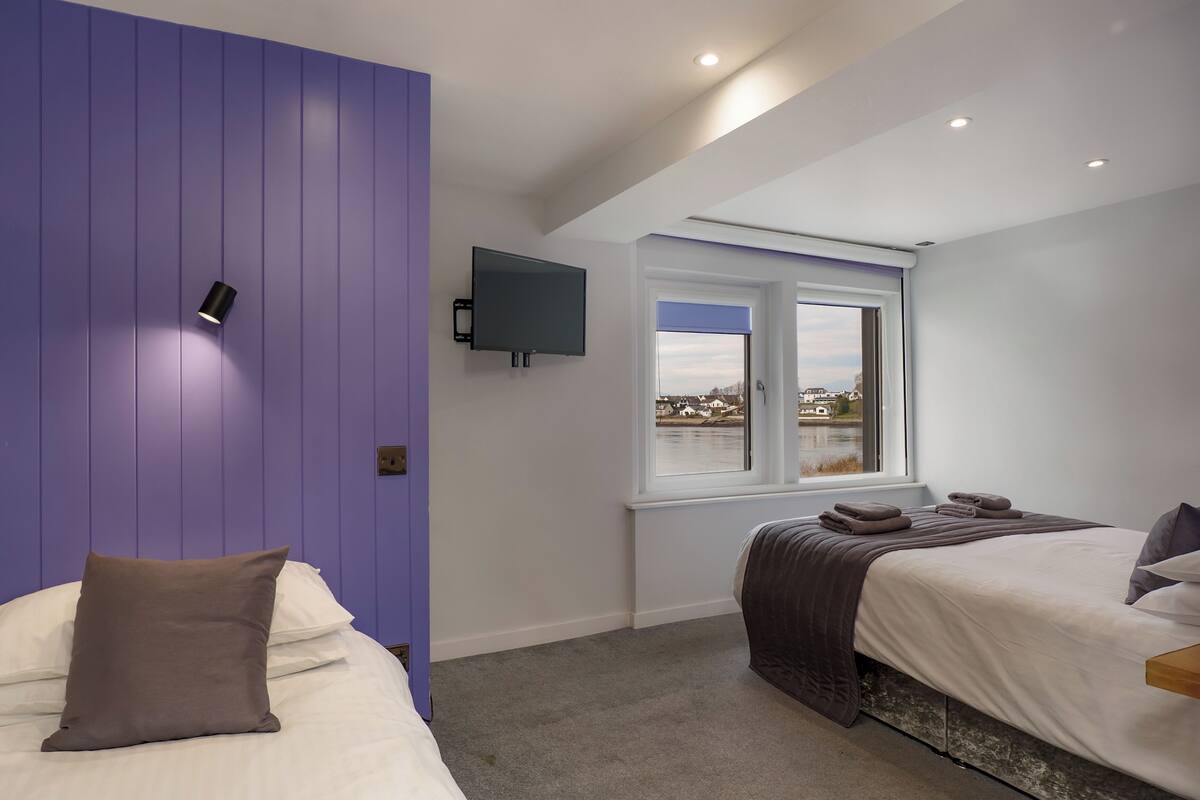 A bedroom with two beds, a TV, and a window with a city view.
