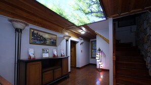 Un pasillo con suelo de madera, una recepción con cuadros enmarcados, una escalera con paredes de piedra y un tragaluz.