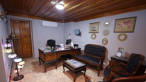Una habitación con un escritorio de madera, un sofá y una mesa de centro. Se observan adornos en la pared y una lámpara.