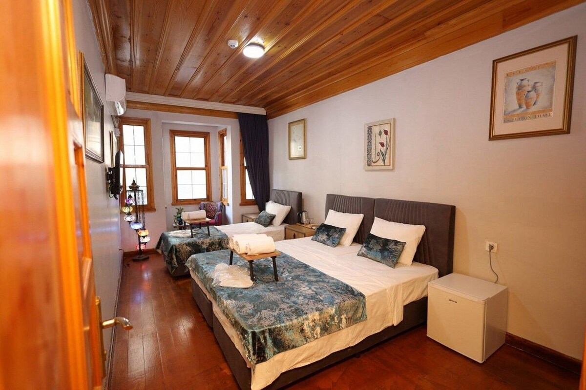 A hotel room with two beds, a small bedside table, a nightstand, and a wall-mounted lamp.