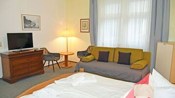 A hotel room with a bed, a television, a desk with a computer, a sofa, a chair, and a lamp.