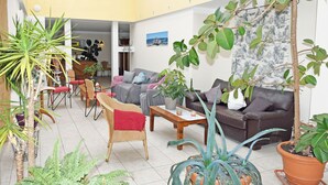 Uma sala de estar ampla com sofá, cadeiras, mesa de centro e diversos vasos de plantas.