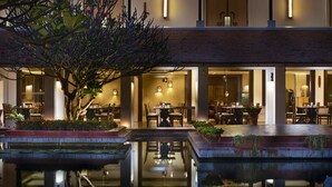 A well-lit outdoor dining area with multiple tables and chairs, surrounded by a water feature and plants. - Sabai Sabai Sukhothai (Sawankhalok)
